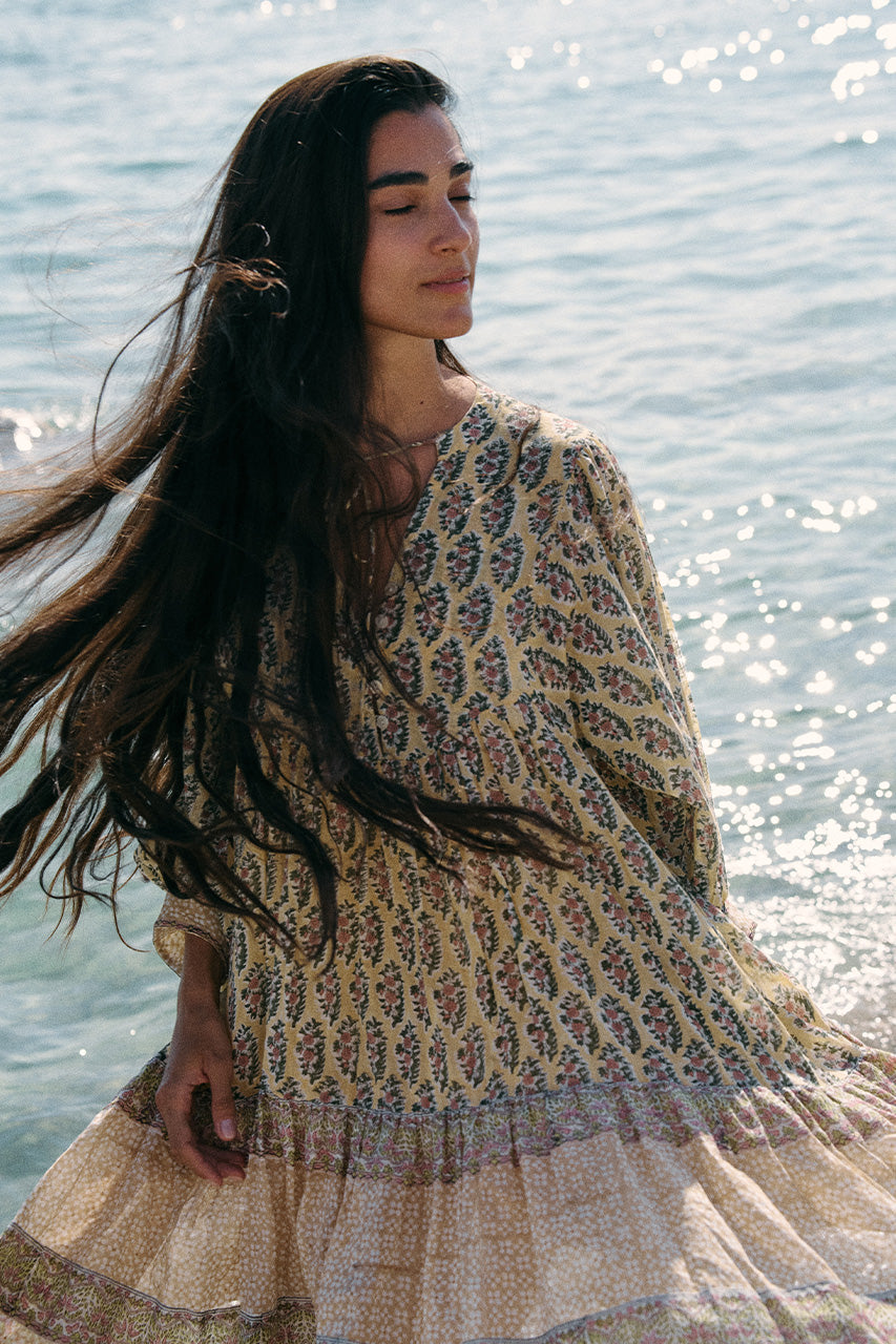 Woman with long flowing hair standing by the sea wearing the Daughters of India Bhoomi Mini Dress in Meadow, the billowed sleeves and tiered skirt captured in natural light