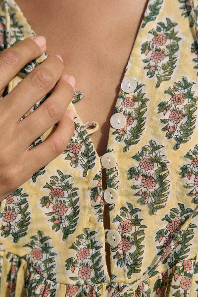 Close-up of V-neckline and button placket on the Daughters of India Bhoomi Mini Dress in Meadow, showing the intricate floral block print fabric on a pale yellow ground