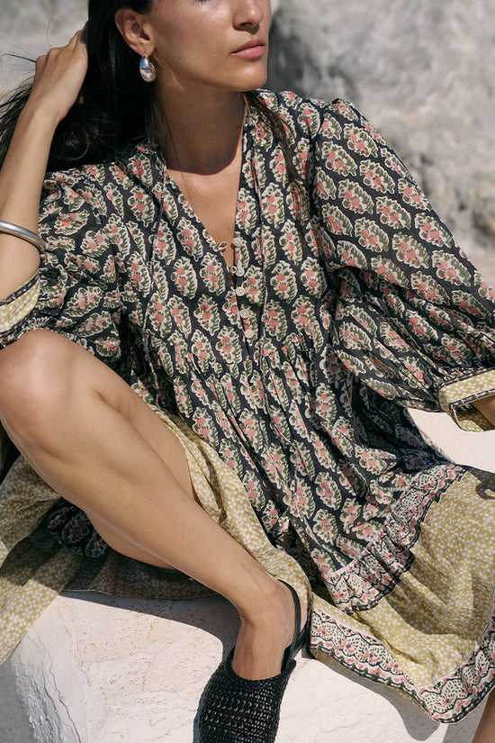 Close-up of woman seated outdoors wearing the Daughters of India Bhoomi Mini Dress in Onyx, showing the detailed paisley block print fabric and tiered skirt with border hem