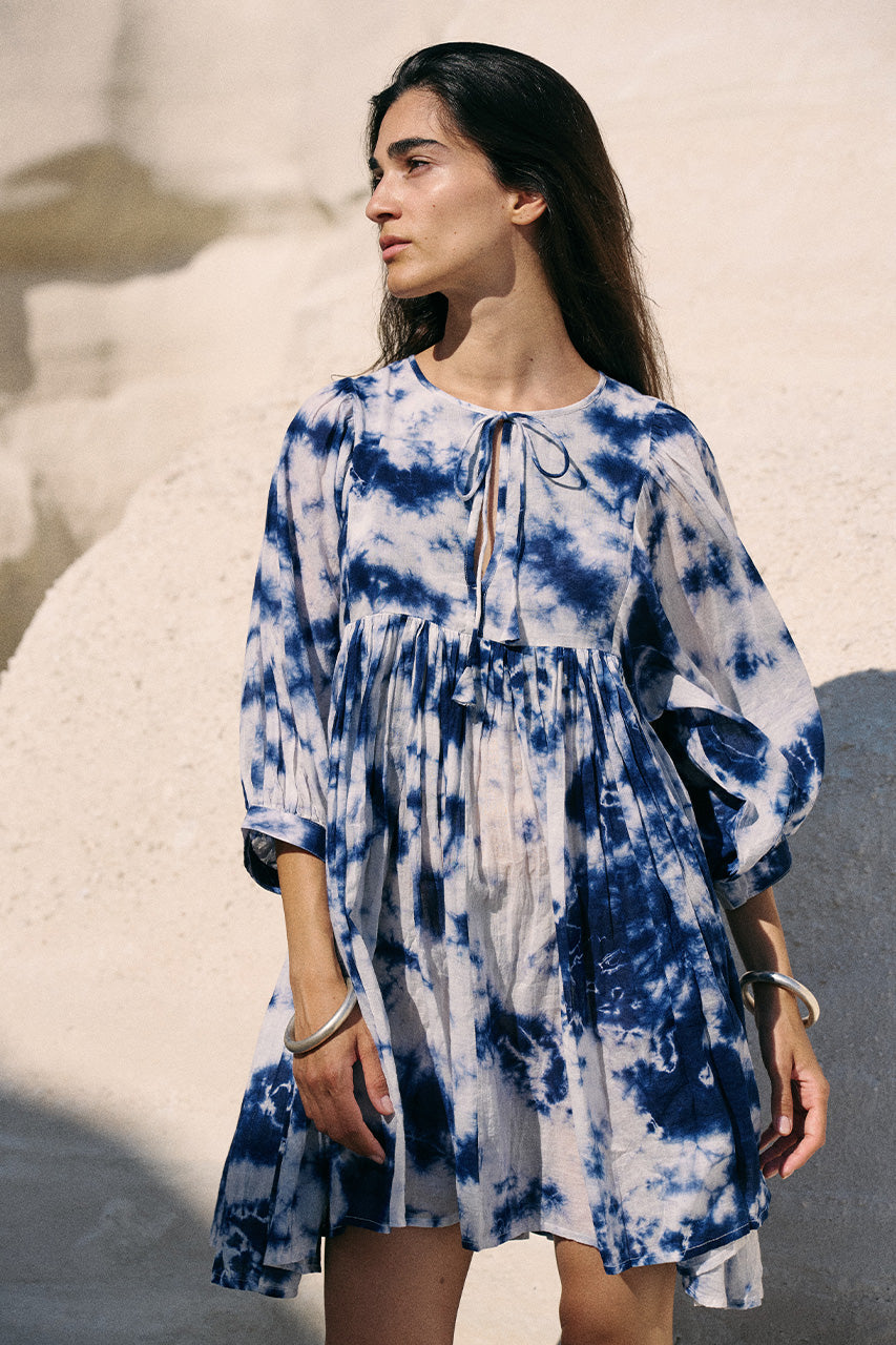 Kyra Mini Dress Deep Sea — full length front view on white sand, deep sea shibori tie-dye cotton mini dress with flowing skirt, bright coastal beach backdrop | Daughters of India