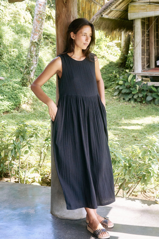 Nadi Dress Black — full length on tropical veranda, black double gauze cotton midi dress with flowing silhouette, bamboo railing and lush greenery | Daughters of India